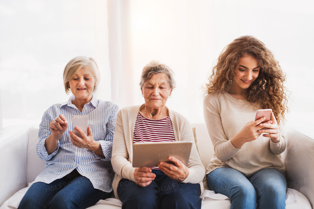 A teenage girl, her mother and grandmother with tablet and smartphones at home. Family and generations concept.