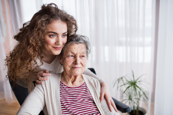 A teenage girl with grandmother at home, hugging. Family and generations concept.