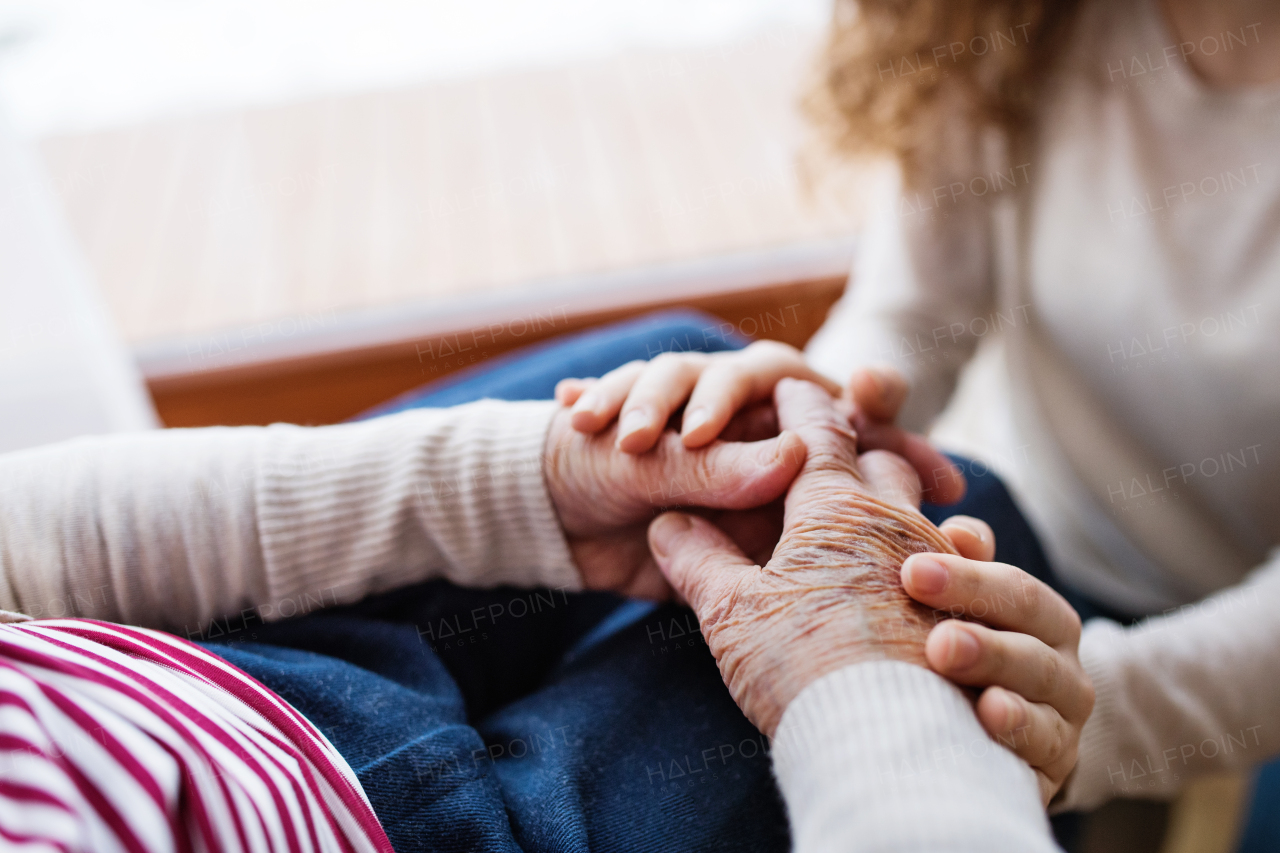 Unrecognizable teenage girl with grandmother at home, holding hands. Family and generations concept. Close up.