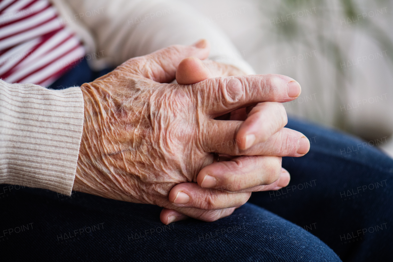 Praying wrinkled hands of a senior woman at home. Close up.