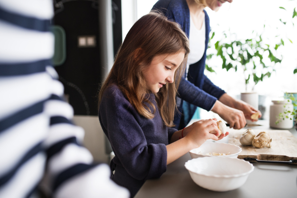 A small girl with unrecognizable mother and grandmother at home, cooking. Family and generations concept.