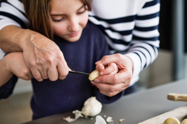 A small girl with her unrecognizable grandmother at home, cooking. Family and generations concept.