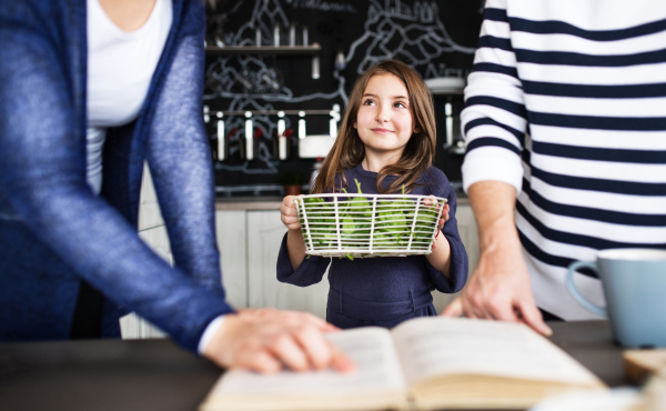 A small girl with her unrecognizable mother and grandmother at home, cooking. Family and generations concept.