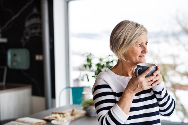 Senior woman in the kitchen. An old woman inside the house, holding a cup of coffee.