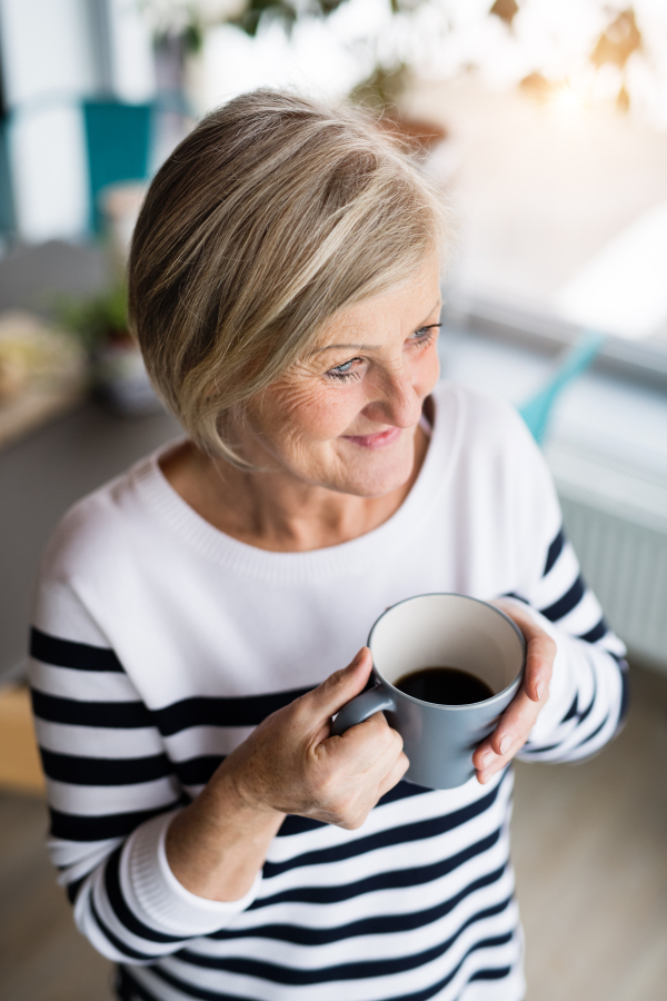 Senior woman in the kitchen. An old woman inside the house, holding a cup of coffee.