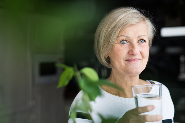 Senior woman in the kitchen. An old woman inside the house, holding a glass of water.