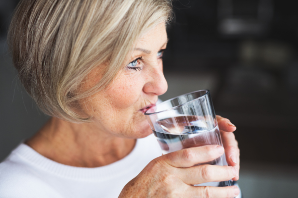 Senior woman in the kitchen. An old woman inside the house, drinking water. Close up.