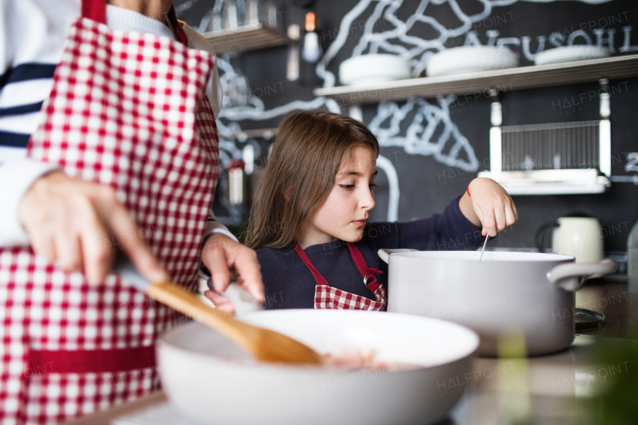 A small girl with unrecognizable grandmother at home, cooking. Family and generations concept.