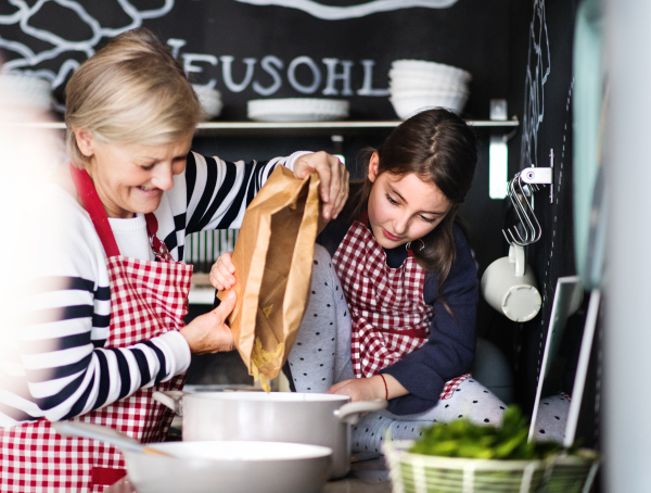 A small girl with grandmother at home, cooking. Family and generations concept.