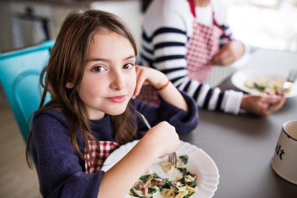 A small girl with unrecognizable grandmother at home, eating. Family and generations concept.