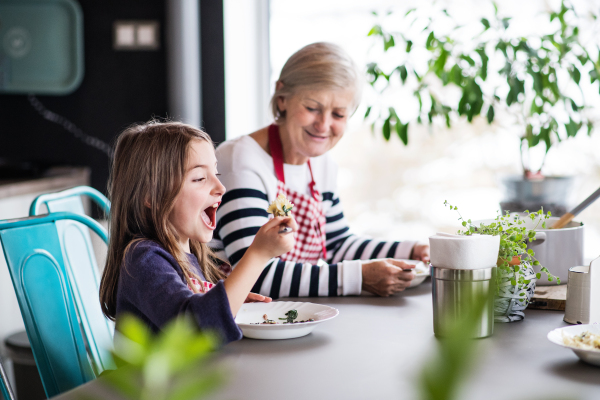 A small girl with grandmother at home, eating. Family and generations concept.