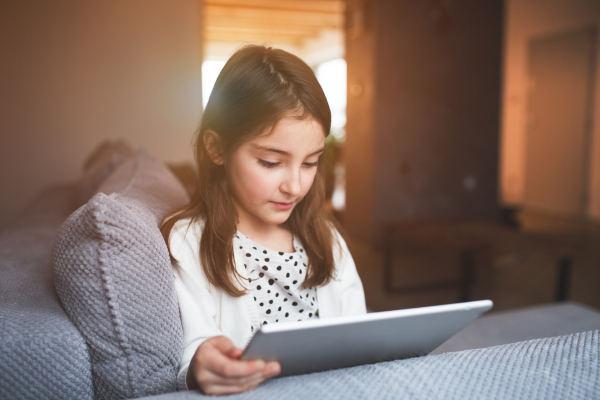 A happy small girl with tablet at home.