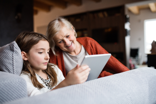 A small girl and her grandmother with tablet at home. Family and generations concept.