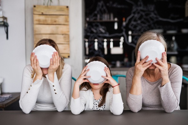 A small girl with her mother and grandmother at home, drinking from a bowl. Family and generations concept.