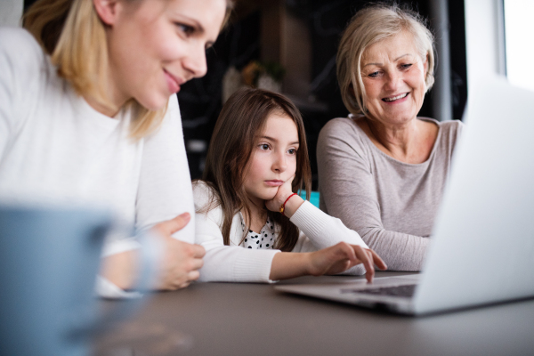 A small girl with laptop and her mother and grandmother at home. Family and generations concept.