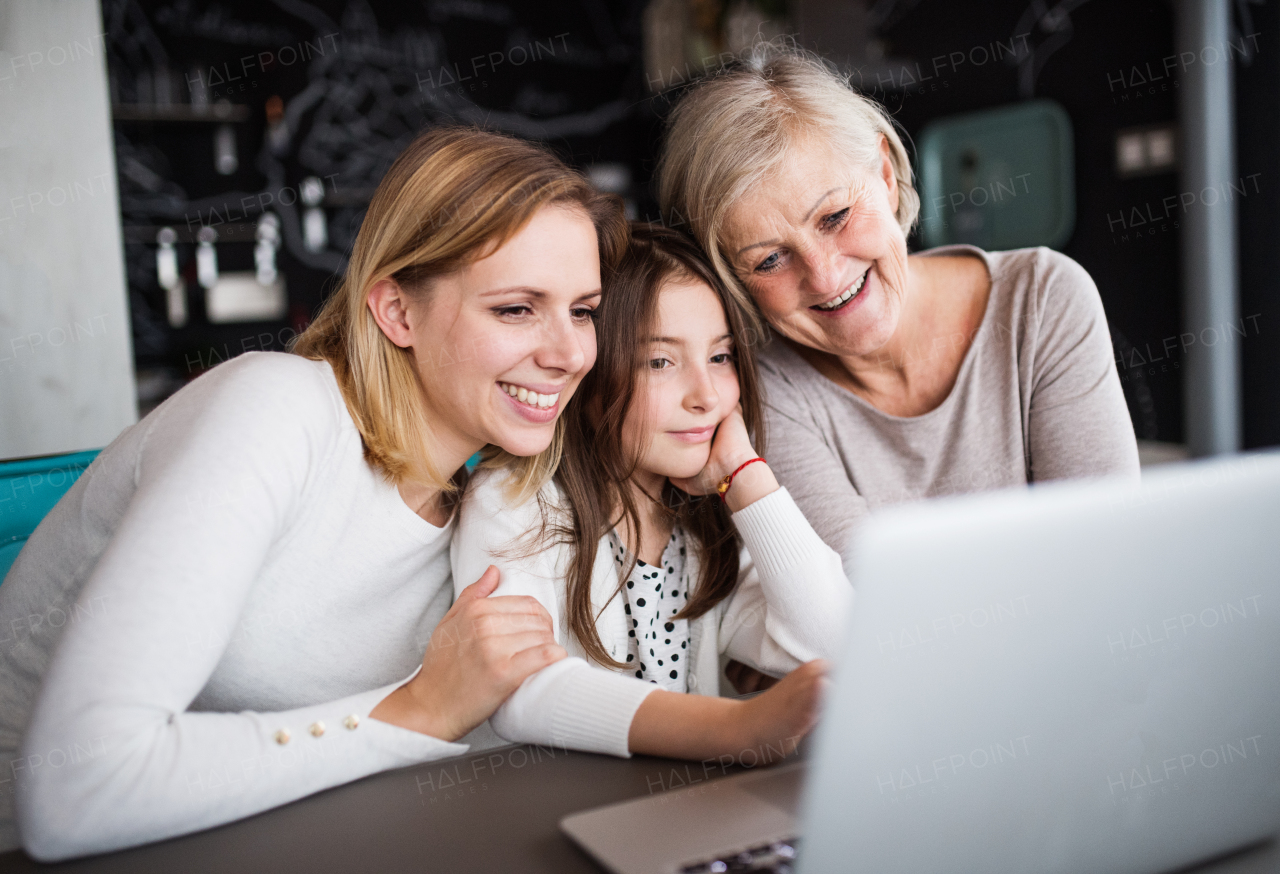 A small girl with laptop and her mother and grandmother at home. Family and generations concept.