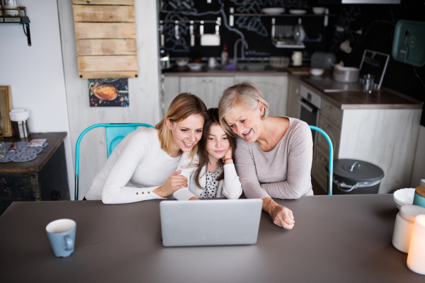 A small girl with laptop and her mother and grandmother at home. Family and generations concept.