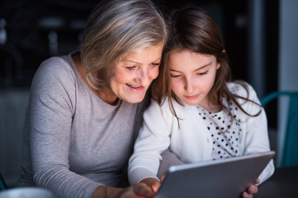 A small girl and her grandmother with tablet at home. Family and generations concept.