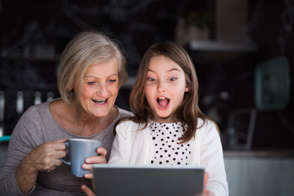 A small girl and her grandmother with tablet at home. Family and generations concept.