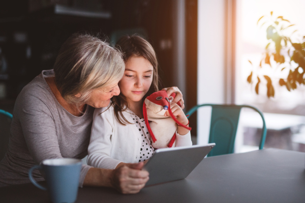 A small girl and her grandmother with tablet at home. Family and generations concept.