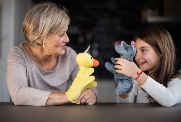 A small girl and her grandmother playing with hand puppets at home. Family and generations concept.