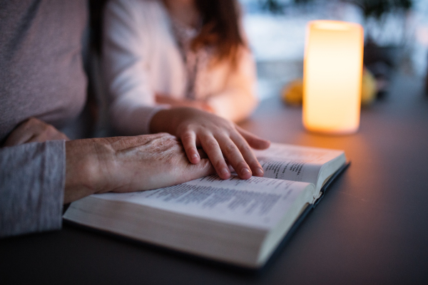 An unrecognizable small girl and her grandmother reading bible at home. Family and generations concept.