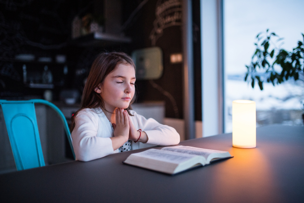 A small girl with bible at home, praying.