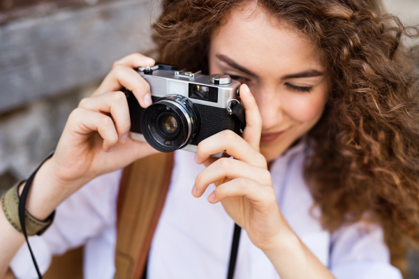 Beautiful young tourist with camera and backpack in the old town, taking a photo.