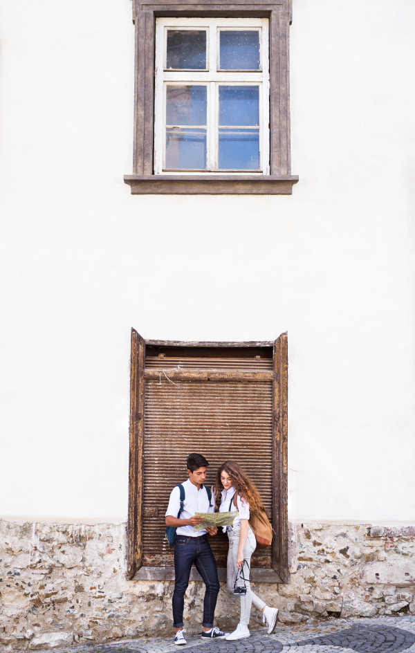 Two beautiful young tourists with map and camera in the old town, next to the wall.