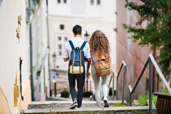 Two beautiful young tourists with backpacks in the old town. Rear view.