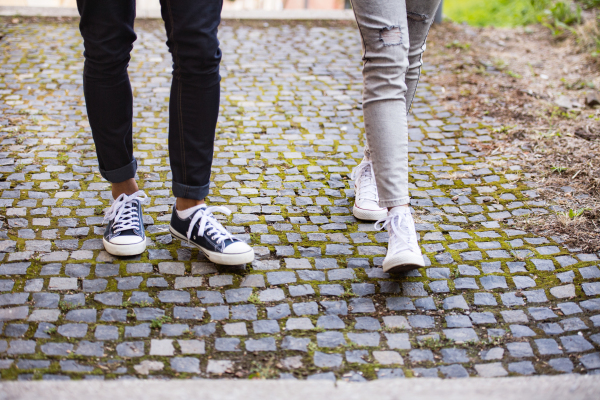 Legs of two unrecognizable young tourists. Teenage girl and boy walking in the old town.