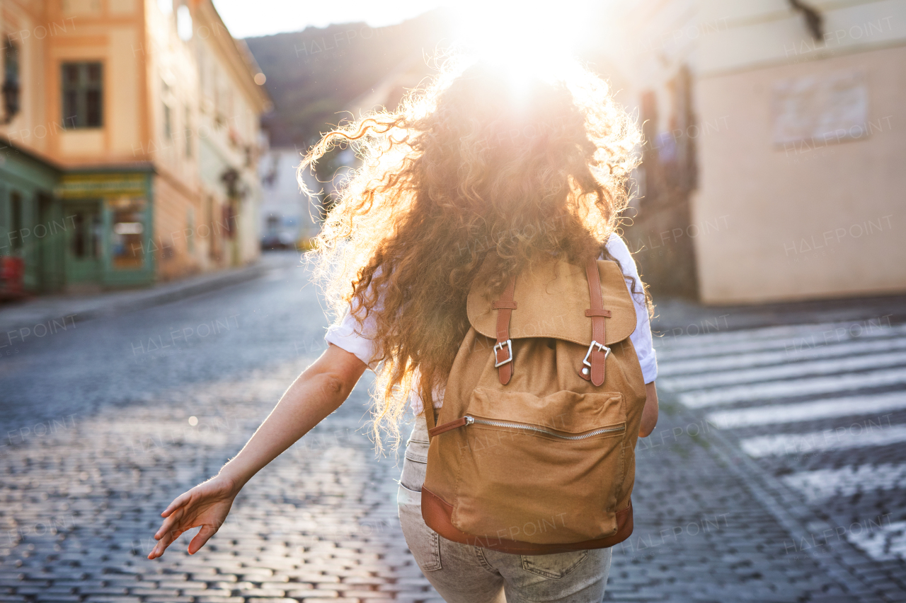 Beautiful young tourist with backpack in the old town. Rear view.