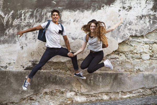 Two beautiful young tourists in the old town having fun. Teenagers jumping against an old wall.