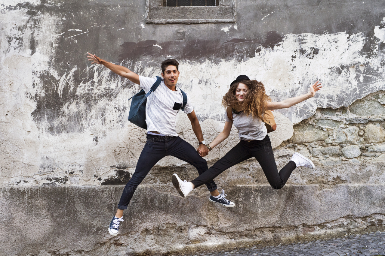 Two beautiful young tourists in the old town having fun. Teenagers jumping against an old wall.