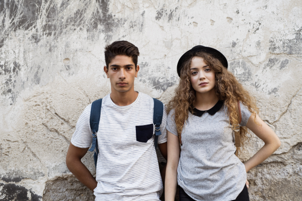 Two beautiful young tourists in the old town leaning against old wall.