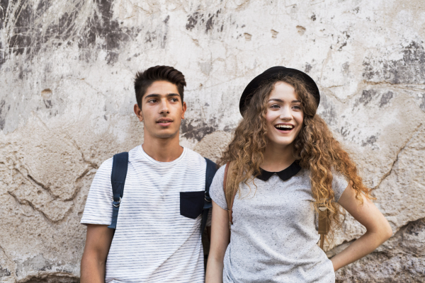 Two beautiful young tourists in the old town leaning against old wall.