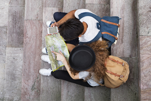 Two young tourists with smartphone and map in the old town. Teenagers sitting on the stairs. top view.