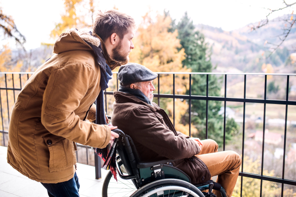 Father in wheelchair and young son on a walk. A carer assisting disabled senior man.