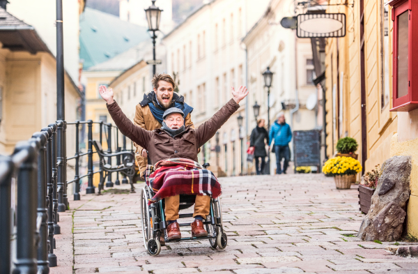 Father in wheelchair and young son on a walk, having fun. A carer assisting disabled senior man.