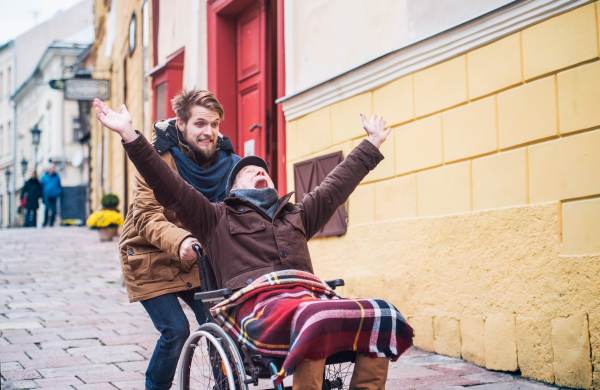 Father in wheelchair and young son on a walk, having fun. A carer assisting disabled senior man.