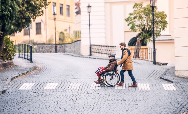 Father in wheelchair and young son on a walk., crossing the road. A carer assisting disabled senior man.