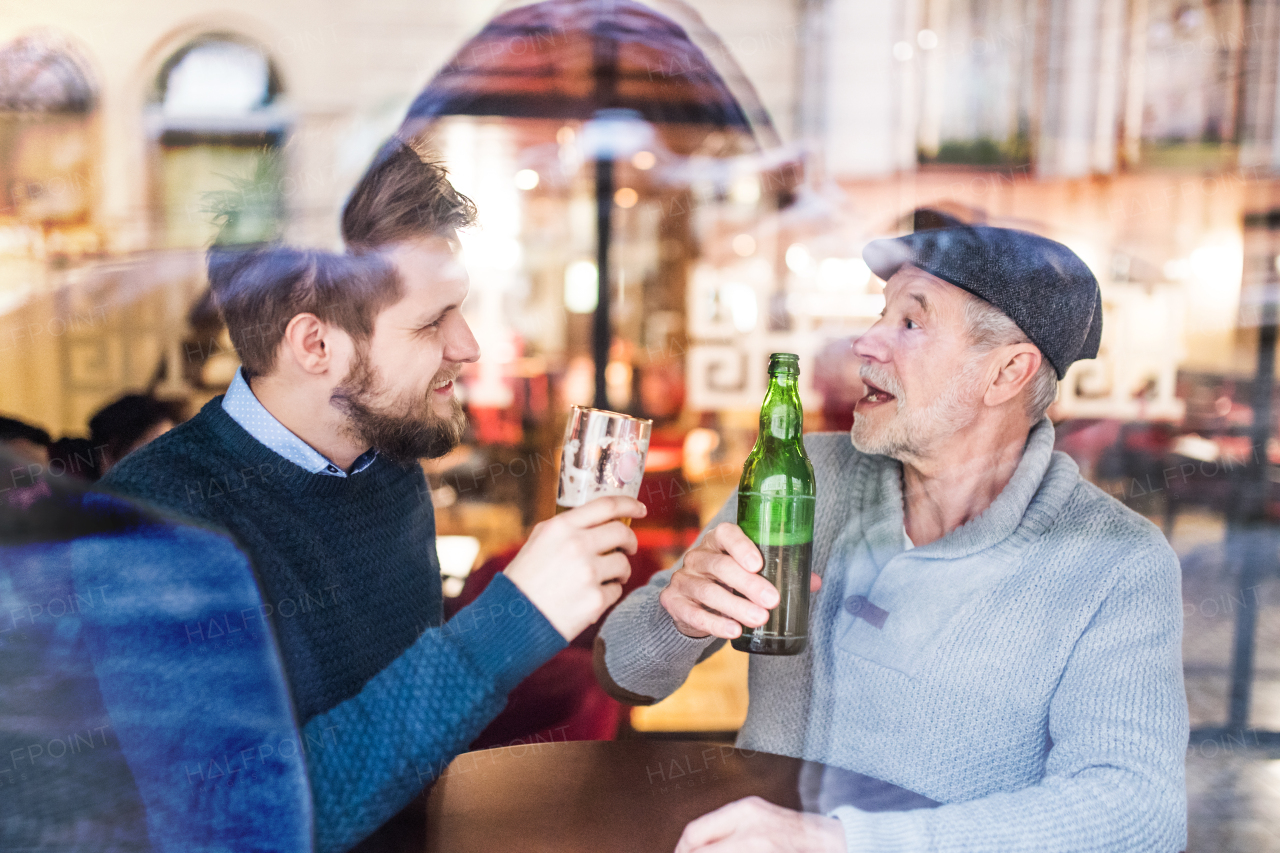 Senior father and his young son drinking beer in a pub. Shot through glass.