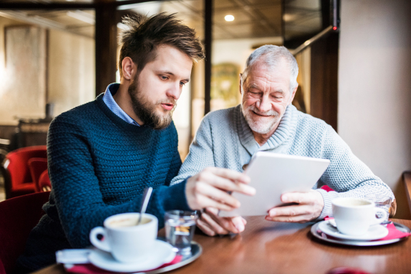 Senior father and his young son with tablet in a cafe.