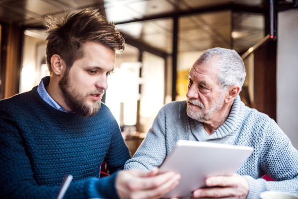 Senior father and his young son with tablet in a cafe.