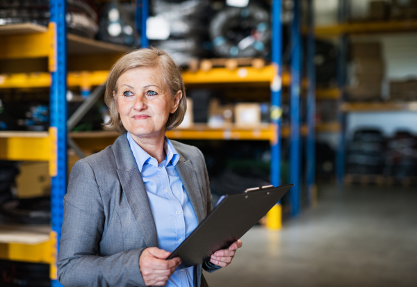 Portrait of a senior woman warehouse manager or supervisor with clipboard. Copy space.