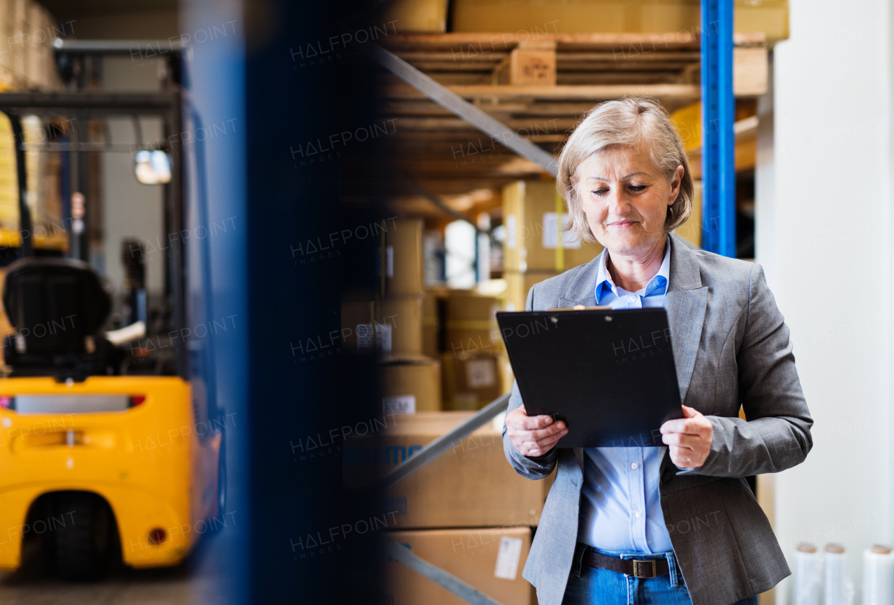 Senior woman warehouse manager or supervisor with clipboard, controlling stock.