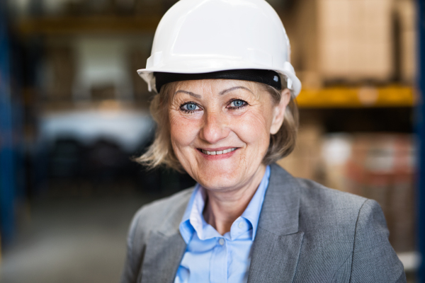 Portrait of a senior woman warehouse manager or supervisor with white helmet. Close up.