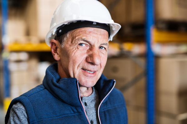 Portrait of a senior male warehouse worker or a supervisor with white hardhat. Close up.