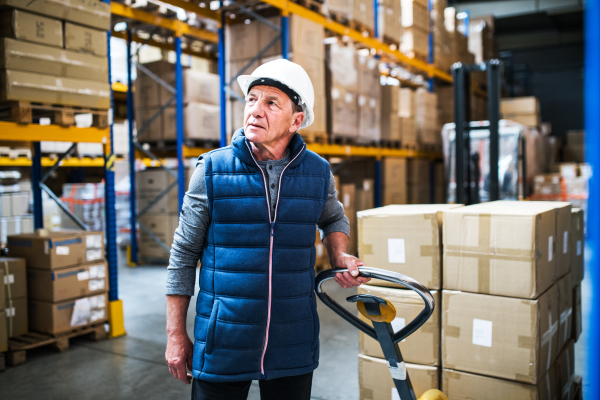 Senior male warehouse worker pulling a pallet truck with boxes.