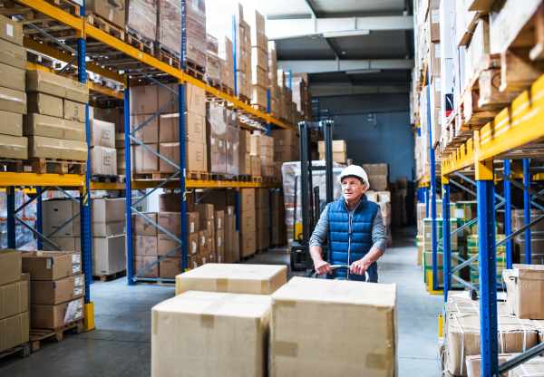 Senior male warehouse worker pulling a pallet truck with boxes.